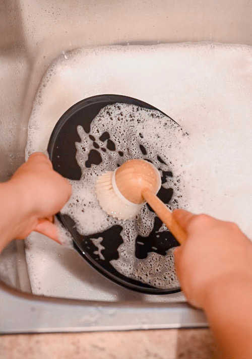 Washing a black plate in a sink with suds from homemade dish soap