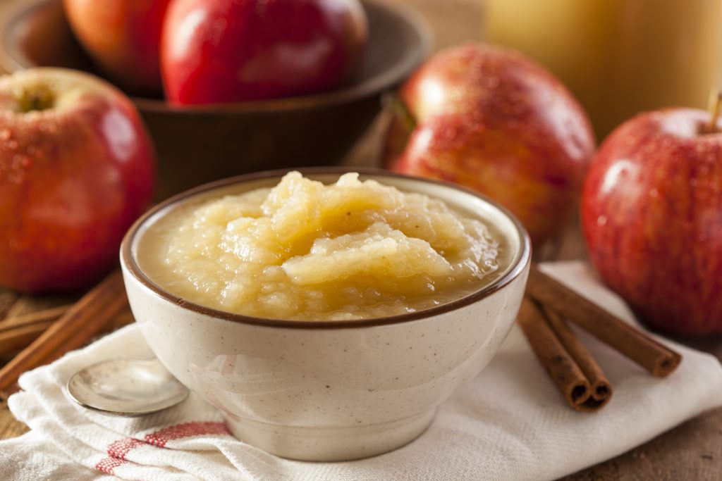 bowl of applesauce on white towel surrounded by apples and a cinnamon stick
